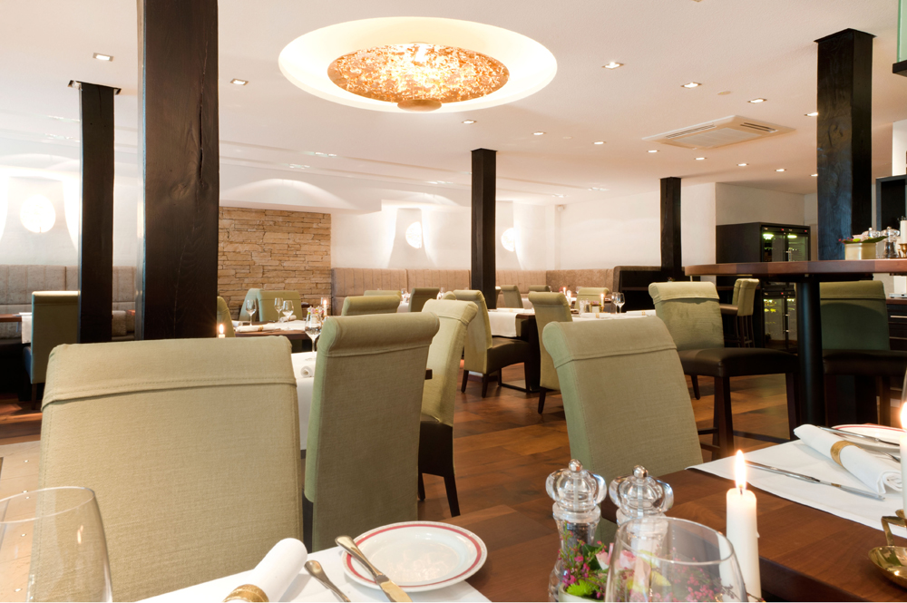 Elegantes Restaurant mit weiß gedeckten Tischen, grünen Stühlen und warmer Beleuchtung, bereit für Gäste.