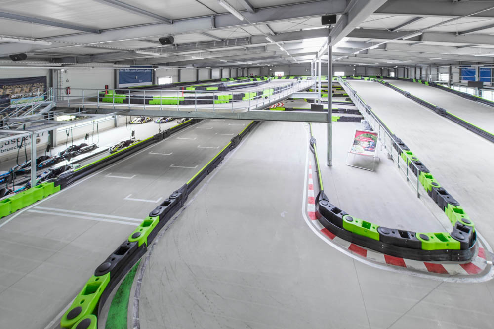 Eine leere Indoor-Kartbahn mit klaren Kurven, grünen und schwarzen Barrieren und geparkten Karts.