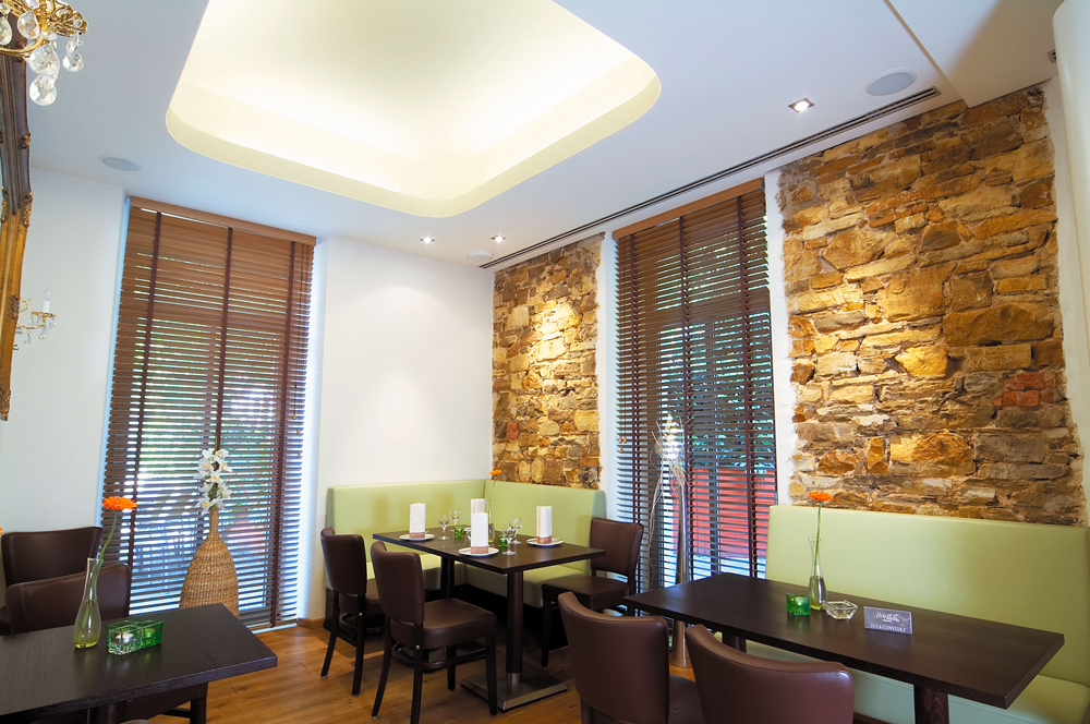 Ein stilvolles Restaurant mit dunklen Holzmöbeln, Natursteinwand und großen Fenstern.