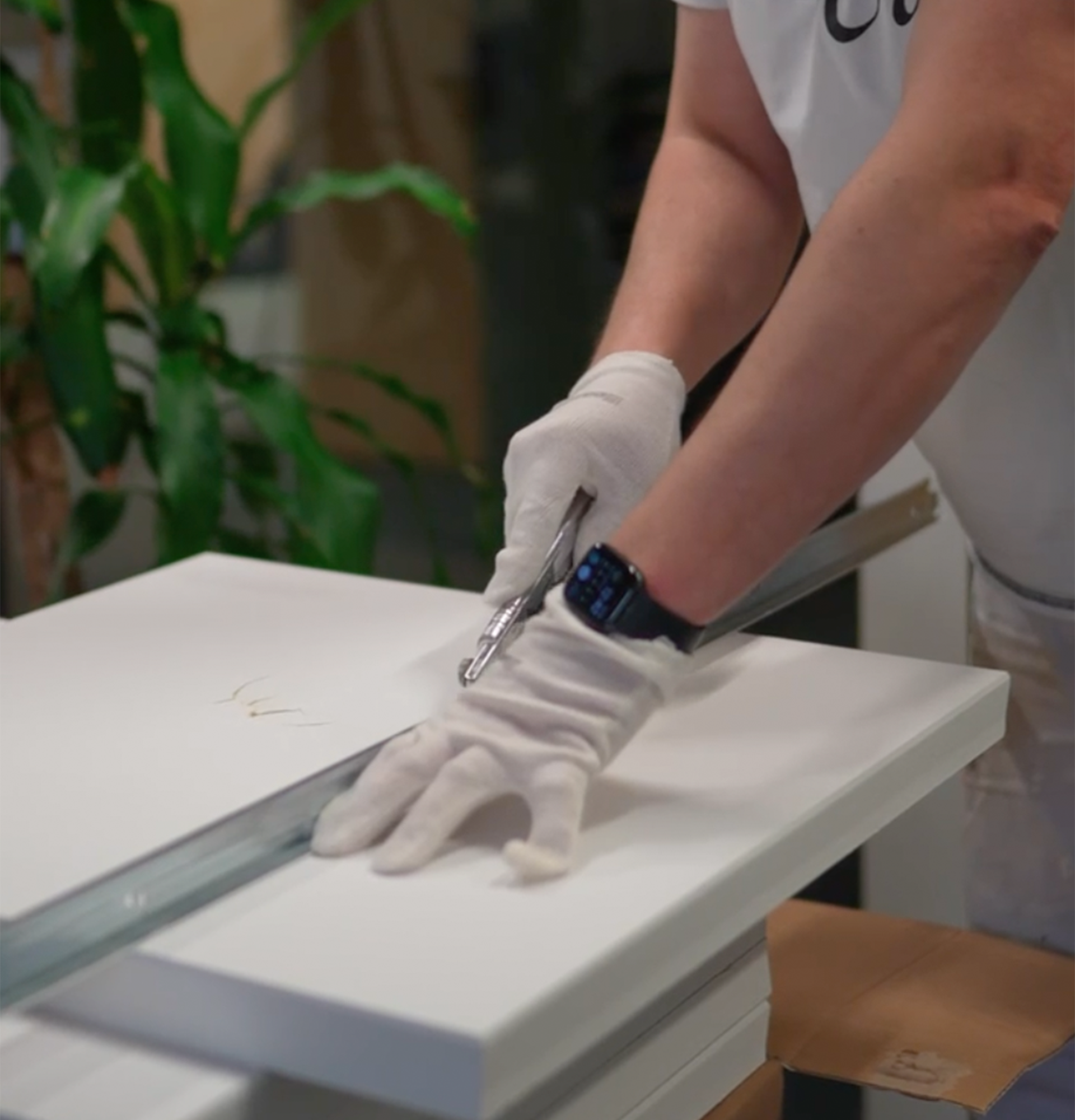 Handwerker mit weißen Handschuhen bearbeitet eine weiße Platte mit Werkzeug