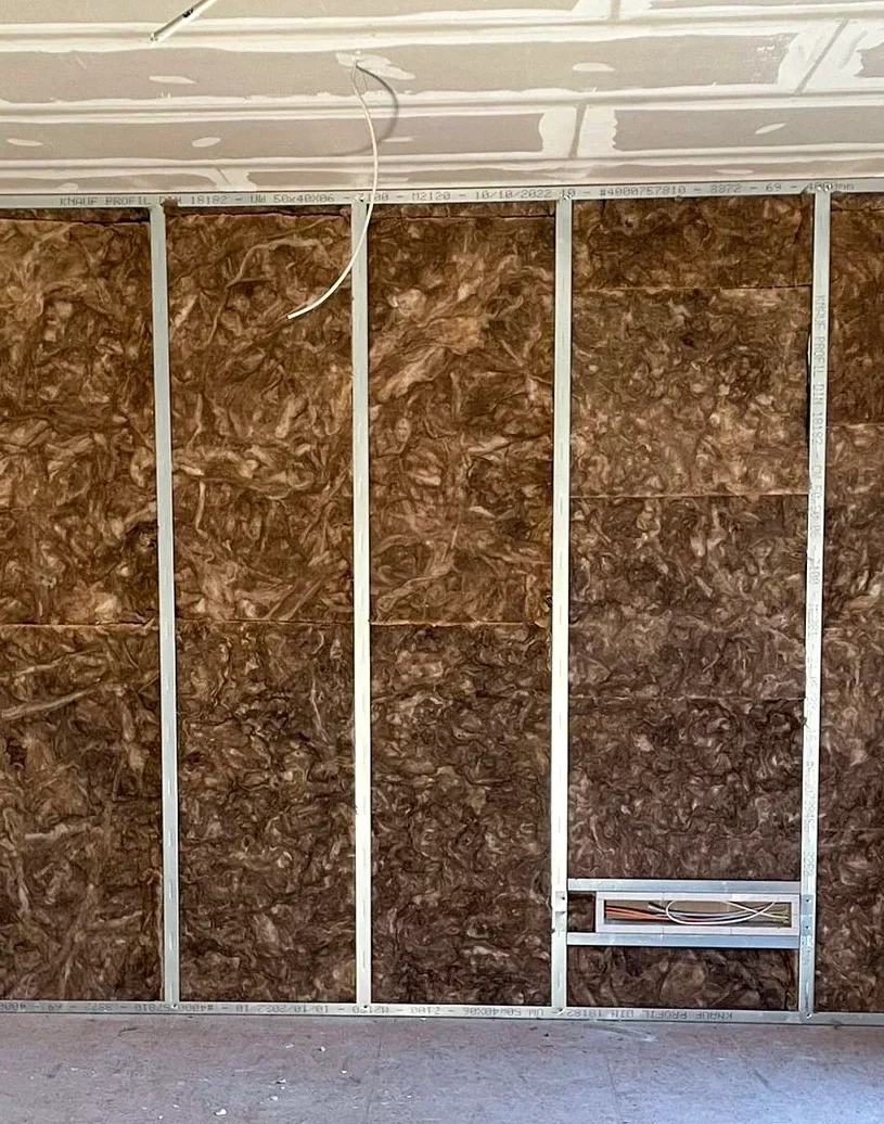 Unvollendete Innenwand mit Metallprofilen, Dämmmaterial und losem Kabel, Baustelle im Ausbauzustand.